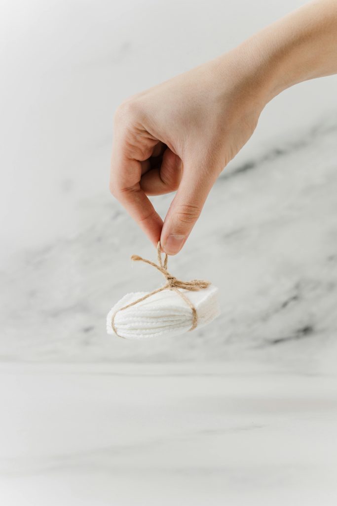 Hand holding eco-friendly cotton pads tied with jute against marble background.